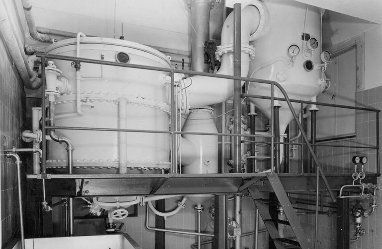 Historical photo of industrial tanks and pipes in a factory.